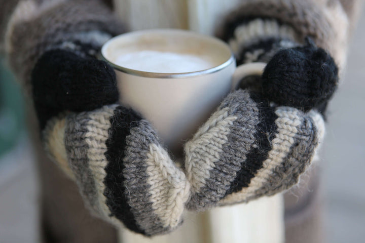 a person with mittens holding a full mug