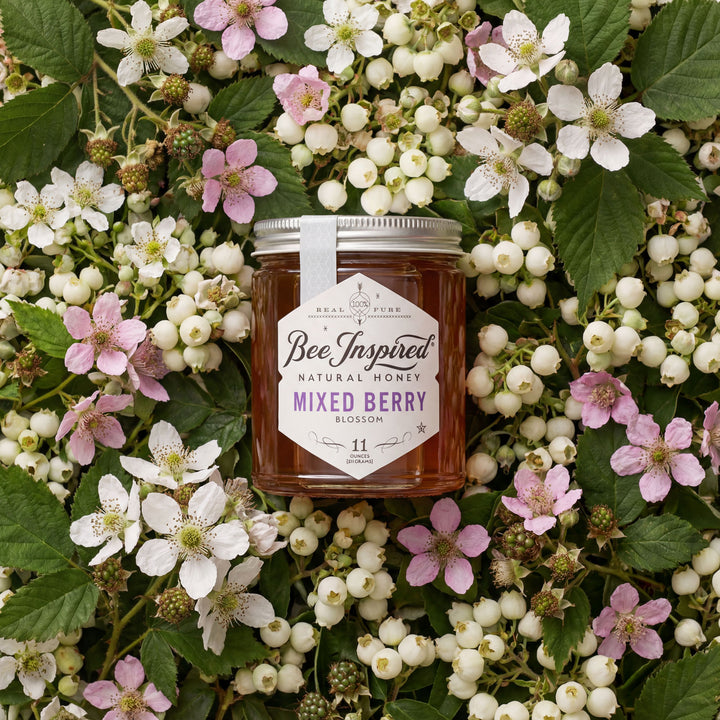 Jar of Bee Inspired honey surrounded by mixed berries and flowers