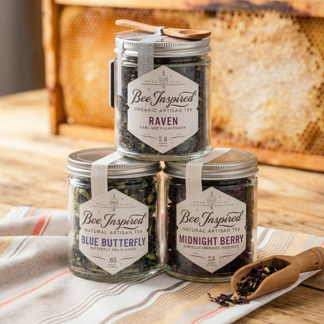 Three jars of 'Bee Inspired' organic artisan tea on a wooden surface with a woven basket in the background.