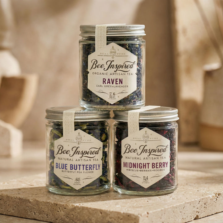Three jars of 'Bee Inspired' organic artisan tea stacked on a stone surface with a blurred background.
