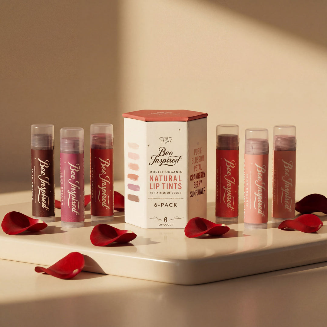 Set of lip tint containers with a box labeled 'Bee Inspired' on a beige surface with red petals.