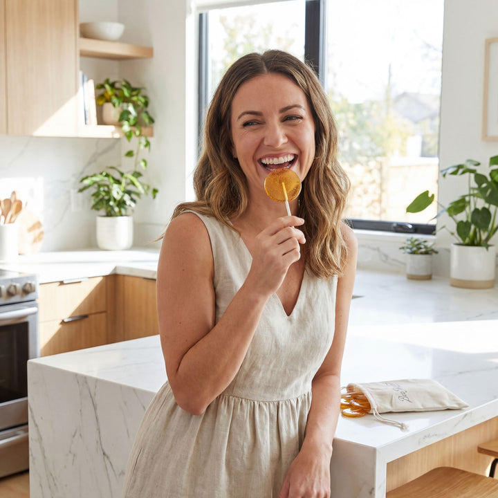 Woman in a kitchen holding a lollipop, smiling.