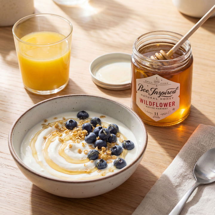 Yogurt bowl with blueberries, a jar of honey, and a glass of orange juice on a wooden table.