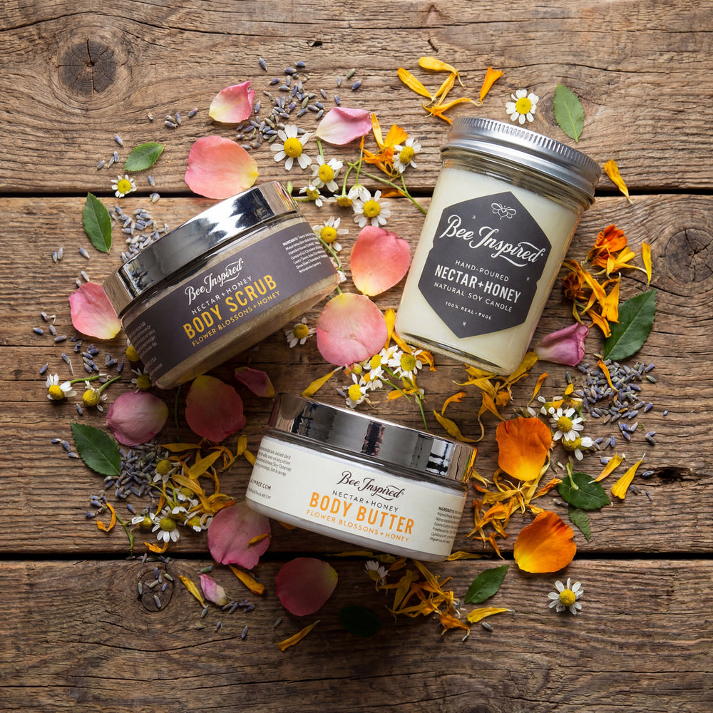 Three containers of 'Bee Inspired' body products on a wooden surface with flowers and petals.