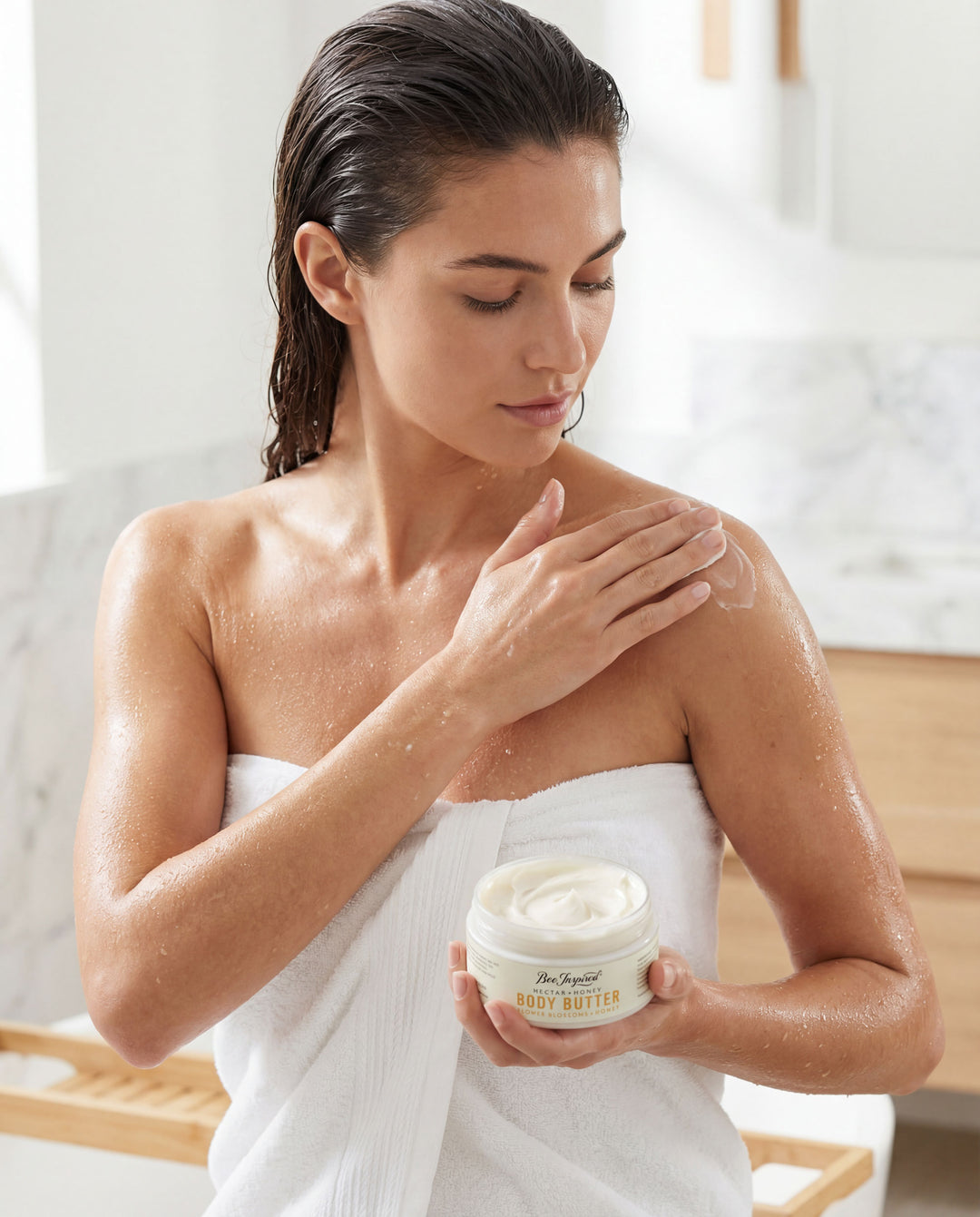Woman applying body butter to her shoulder in a bathroom setting