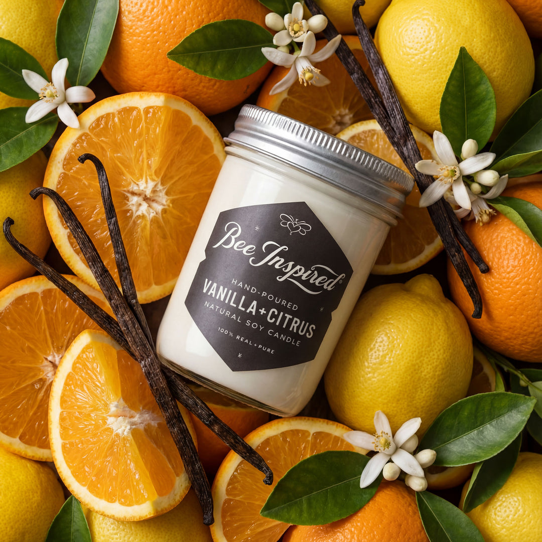 Jar of 'Bee Inspired' vanilla citrus candle surrounded by oranges, lemons, and vanilla beans.