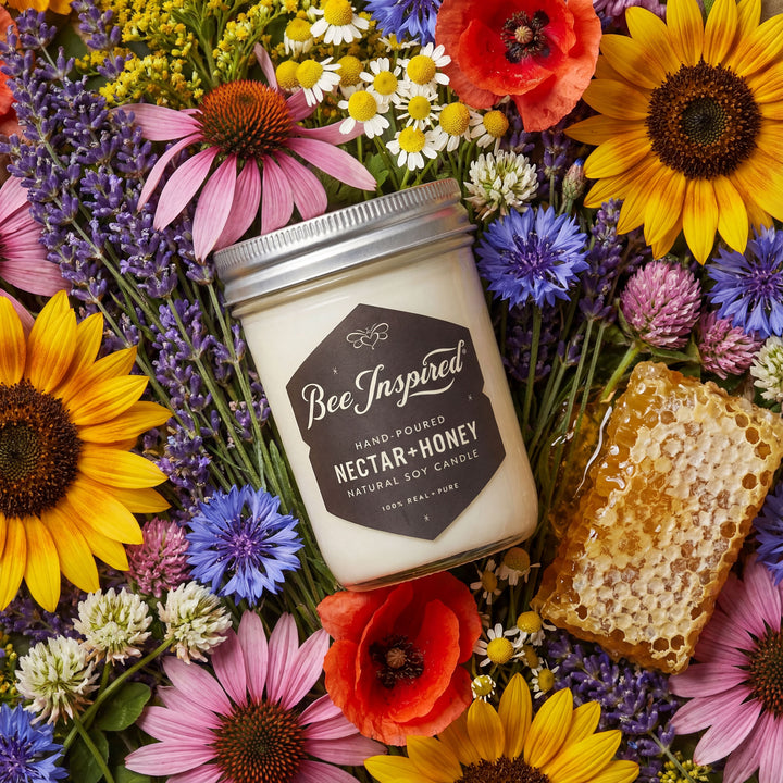 Candle labeled 'Bee Inspired' surrounded by flowers and honeycomb