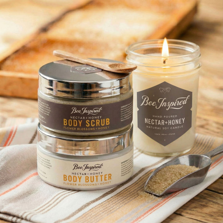 Bee Inspired body care products including a jar of body scrub, body butter, and a candle on a wooden surface.