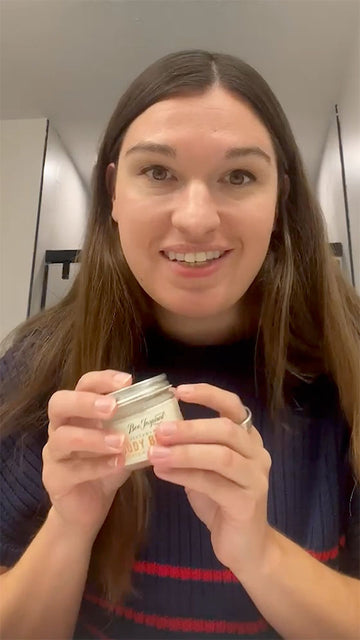 Person holding a small container with a label, standing in a bathroom.