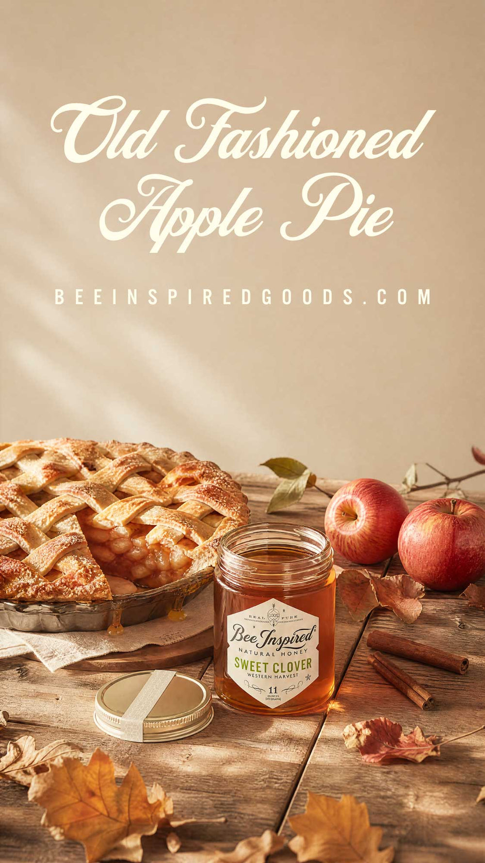 An autumn-themed promotional graphic for 'Old Fashioned Apple Pie' by Bee Inspired Goods. The scene features a golden-brown apple pie on a rustic wooden table alongside fresh red apples, cinnamon sticks, and scattered fall leaves, with a jar of honey in the foreground.