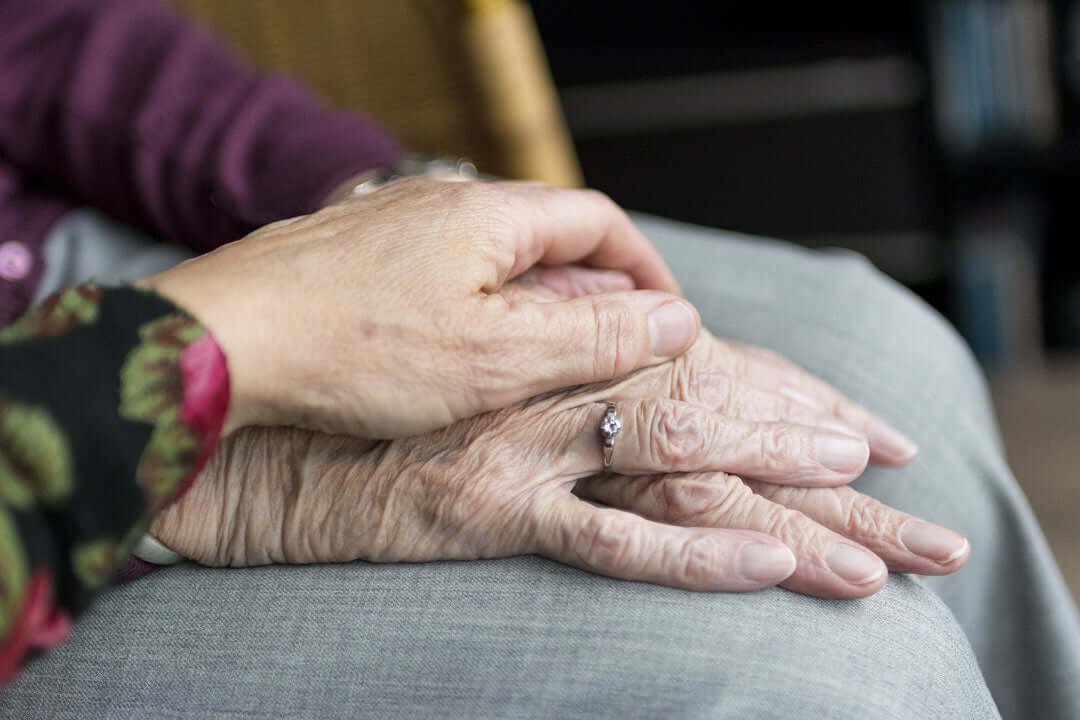 a woman holds her elder mother's hands 