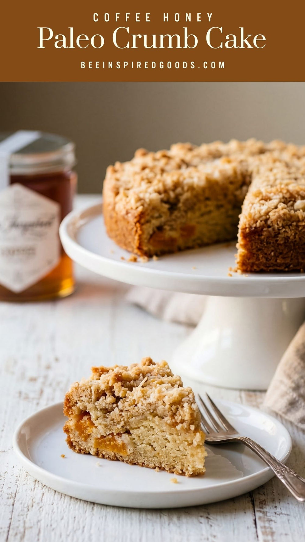 Slice of Paleo crumb cake on a plate with a jar of honey and the cake on a stand in the background.