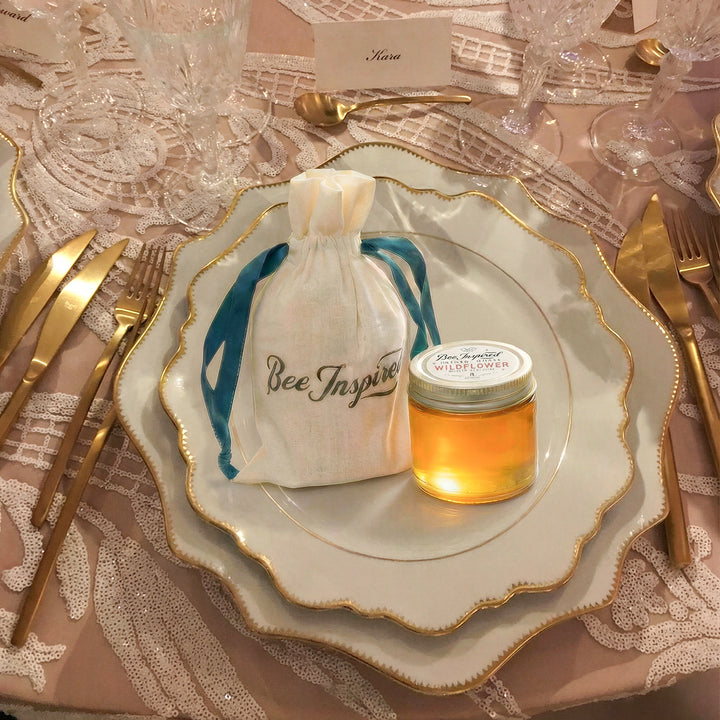 Wedding table setting with a honey favor and a drawstring bag on a decorative plate.

