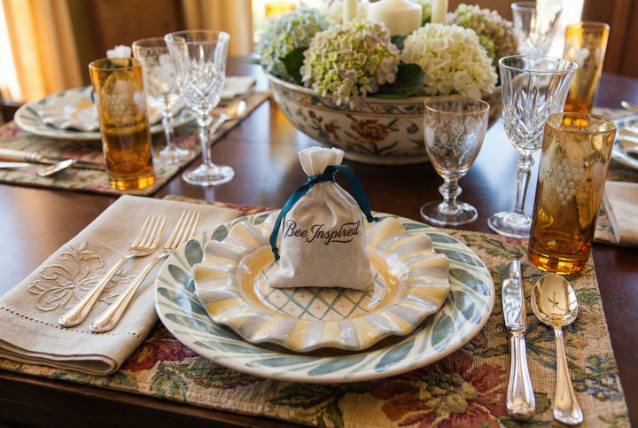 Bee Inspired Party Favor on dining table setting with plates, glasses, and a decorative bag on a floral tablecloth.