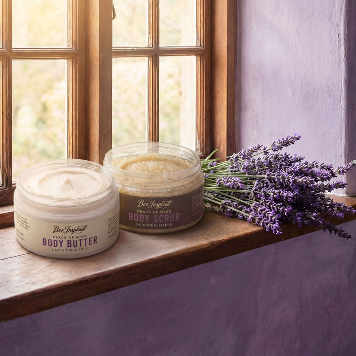 Two jars of Bee Inspired body products on a windowsill with lavender flowers.