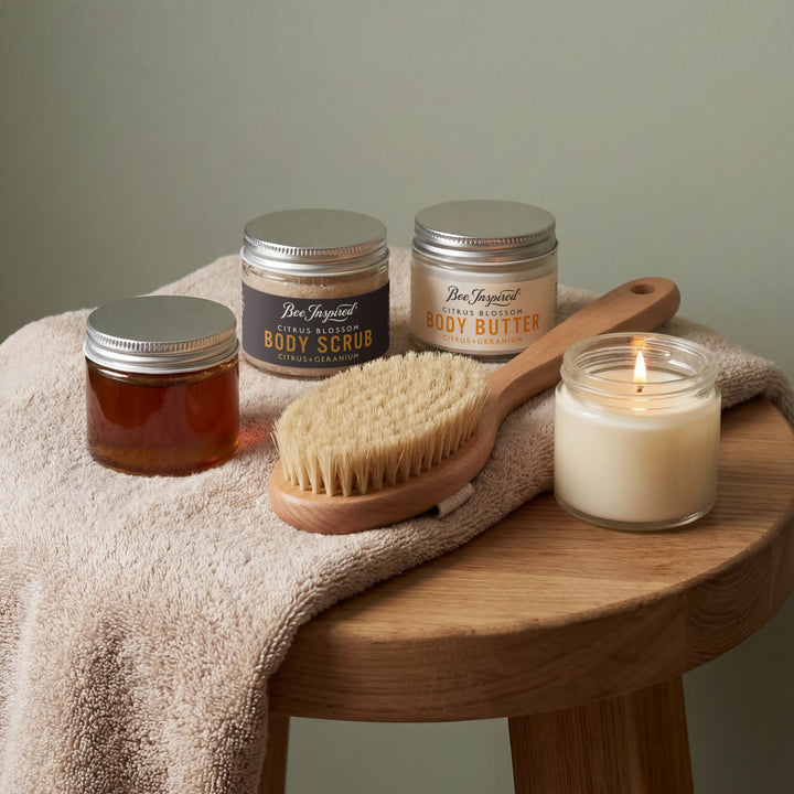 Bath and body products including jars, a candle, and a brush on a wooden surface with a towel.