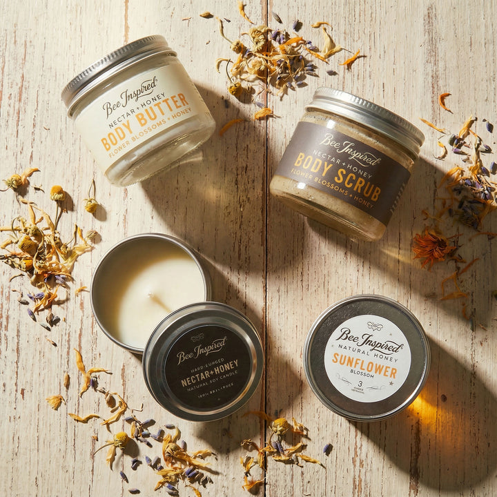 Four containers of Bee Inspired body products on a wooden surface with dried flowers.
