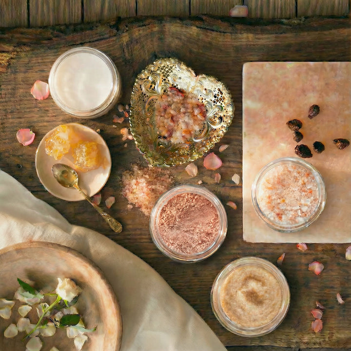 Various skincare products on a wooden surface with rose petals and a gold spoon.