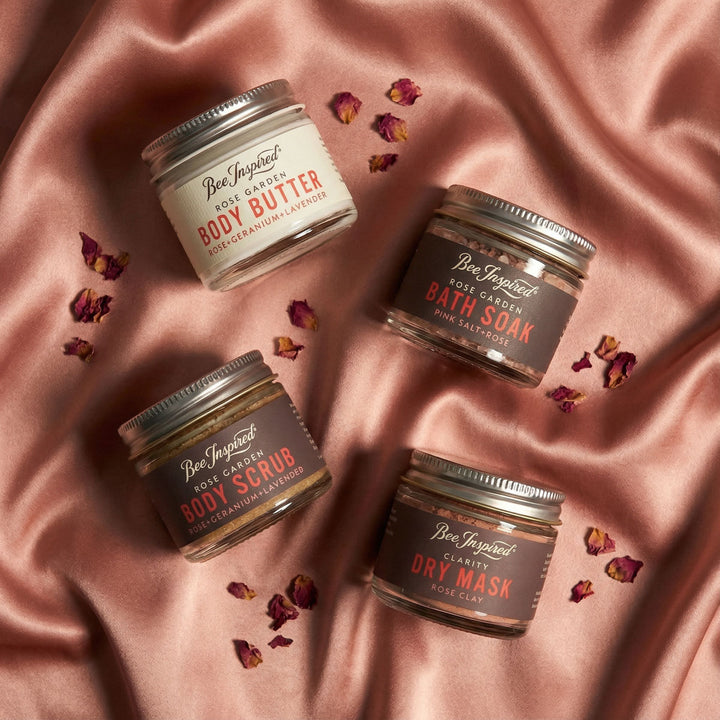 Four small jars of body care products on a pink satin background with dried flowers.
