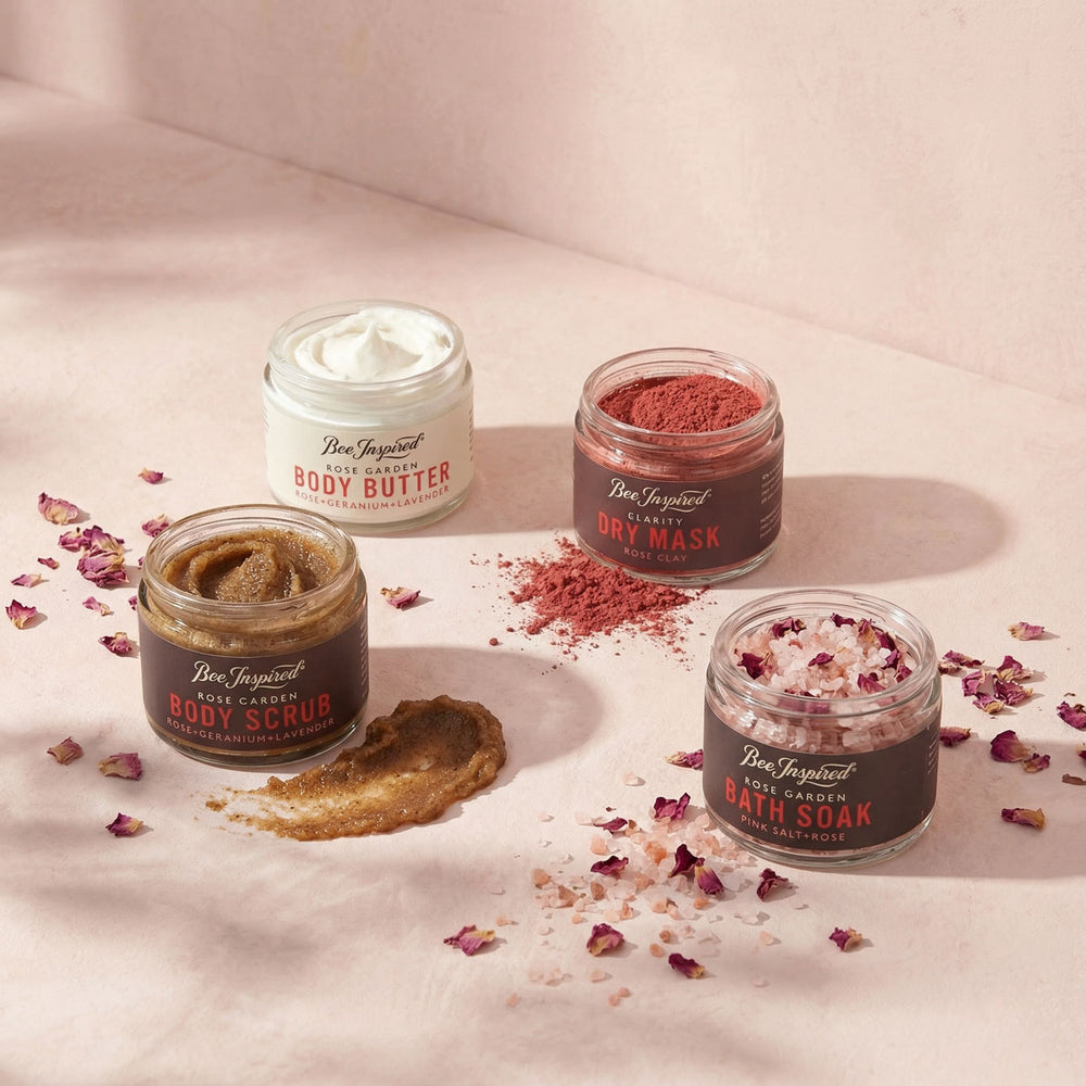 Four jars of Bee Inspired body care products on a light pink background with scattered rose petals.