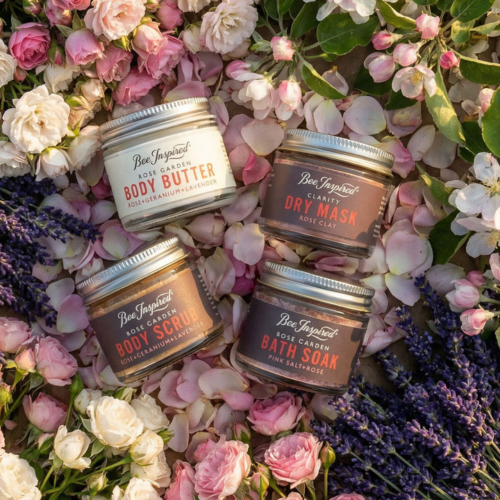 Four jars of 'Bee Inspired' body care products surrounded by flowers on a bed of flowers.