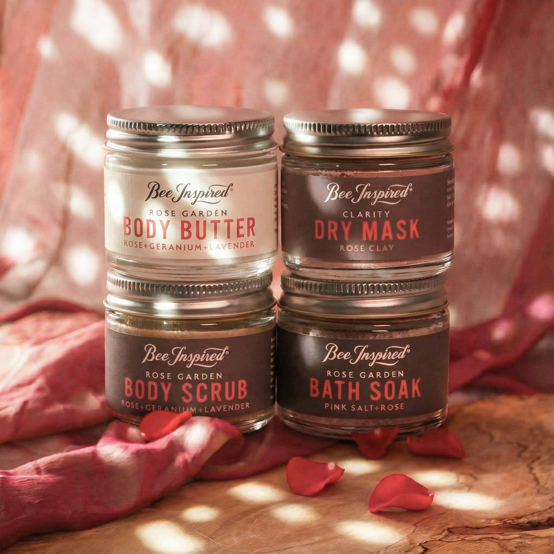 Four jars of Bee Inspired beauty products on a wooden surface with pink fabric in the background.