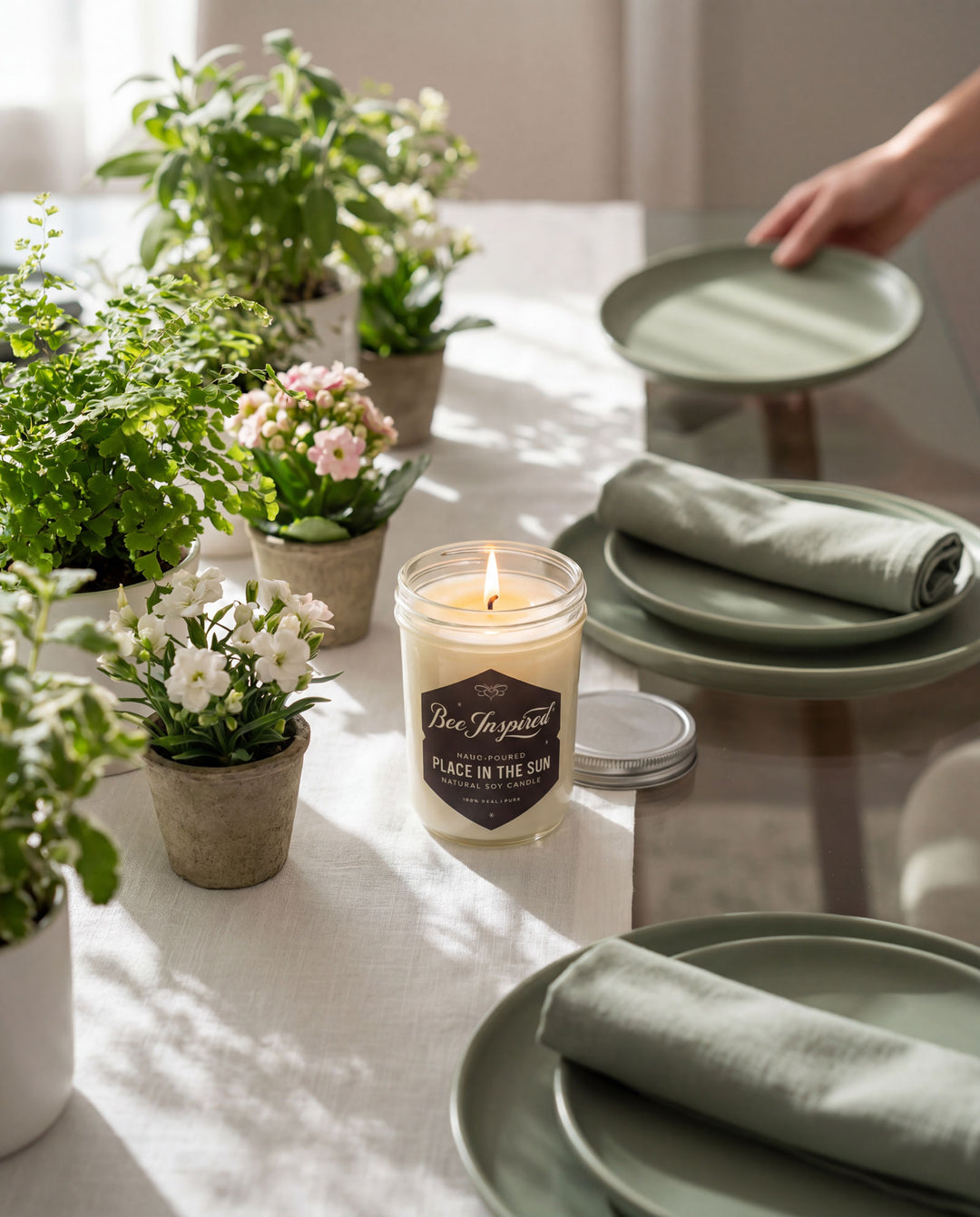 Candle with a label on a table surrounded by potted plants and green plates.