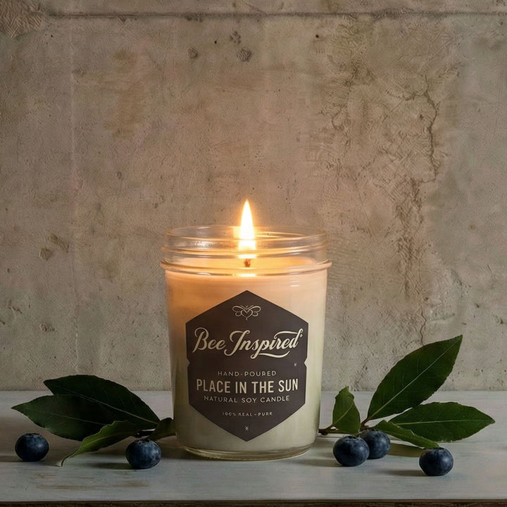 Candle in a jar with 'Bee Inspired' label on a stone surface with leaves and berries.