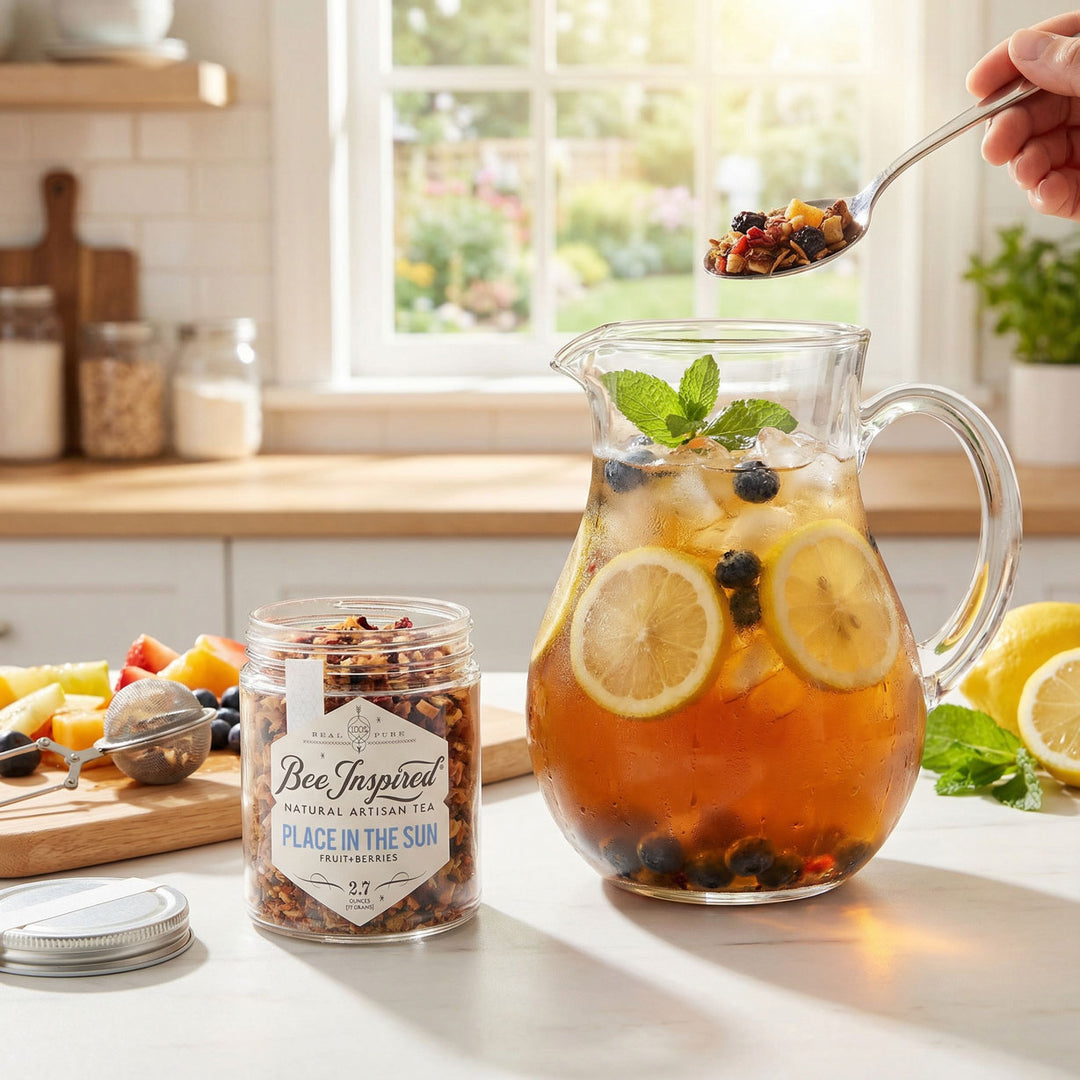 Ice tea pitcher with fruit and tea, jar of Bee Inspired Place in the Sun Tea and spoonful of fruit tea on a kitchen counter.

