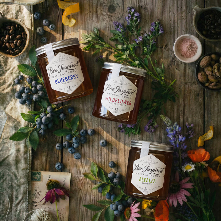 Three jars of Bee Inspired honey on a wooden surface with flowers and berries.