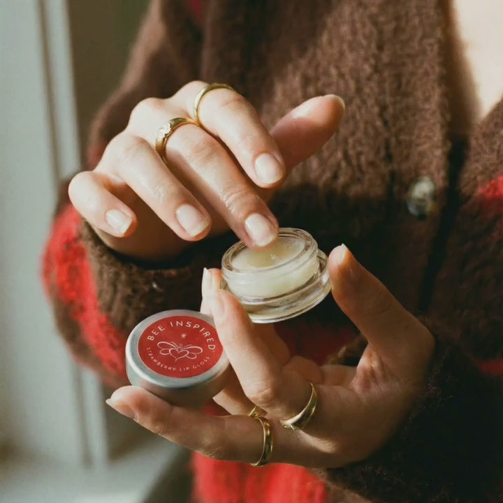 Woman dipping her finger into Bee Inspired Strawberry Lip Gloss to apply.
