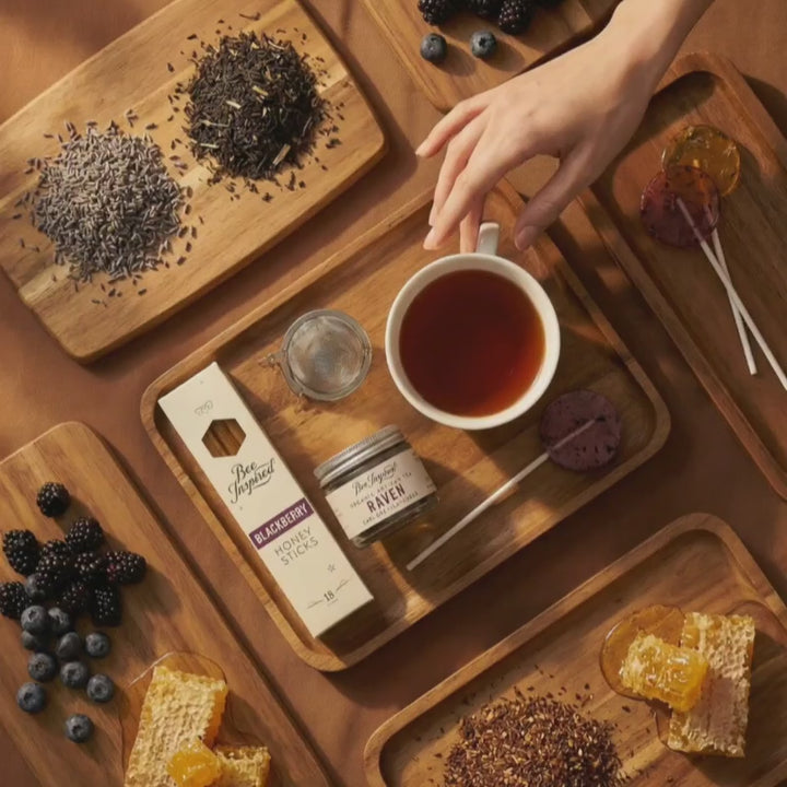 Hand picking up a cup of tea surrounded by products from the Tea and Honey Gift Set.