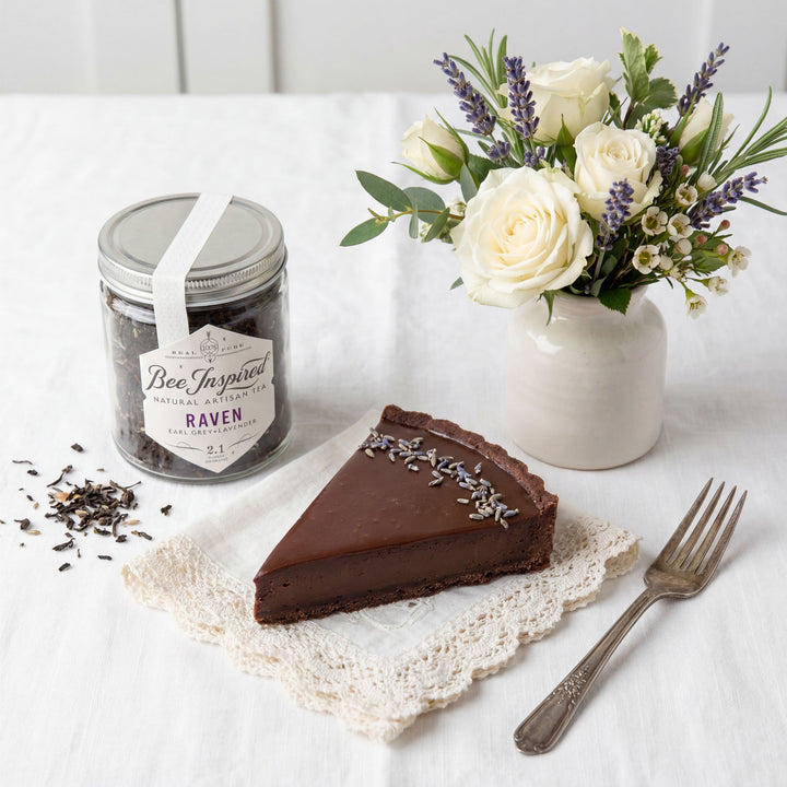 Chocolate tart with lavender, a jar of tea, and a bouquet of flowers on a white surface.