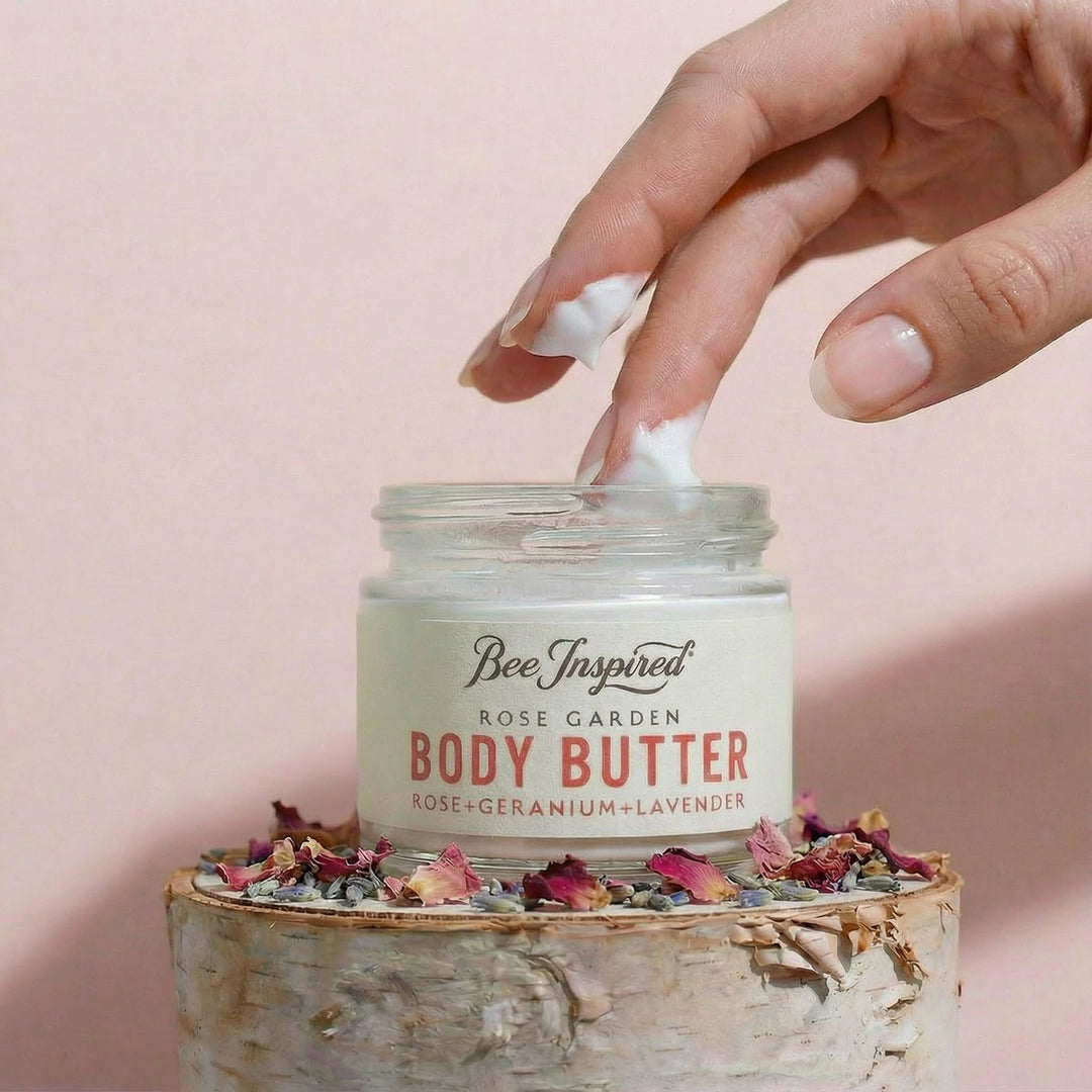 Hand applying body butter from a jar labeled 'Bee Inspired' on a pink background