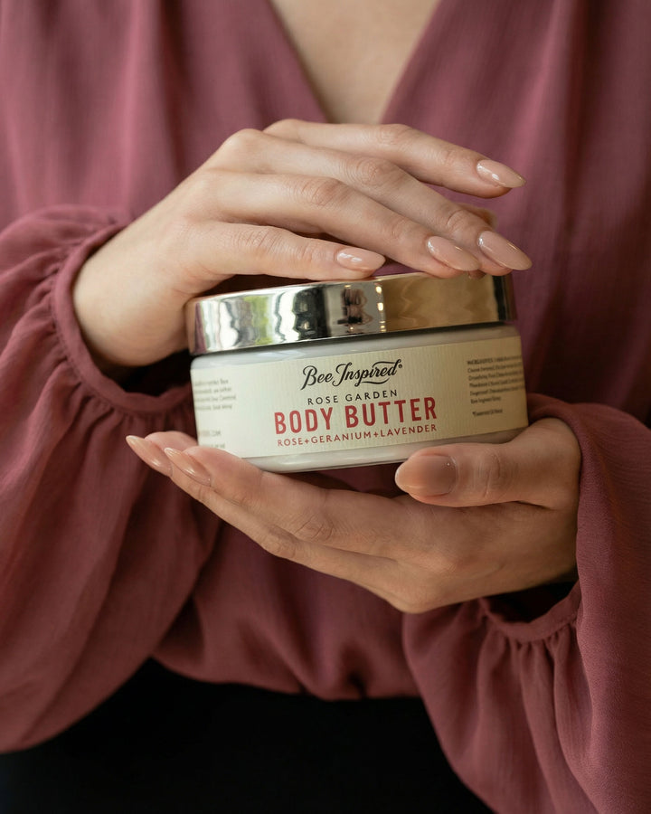 Person holding a jar of 'Rose Garden' body butter with a blurred background