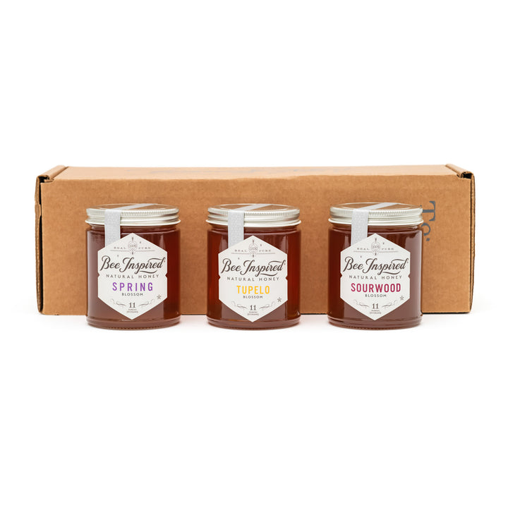 Three jars of 'Bee Inspired' honey with labels in front of a cardboard box on a white background