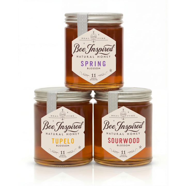 Three jars of 'Bee Inspired' natural honey with different flavors on a white background
