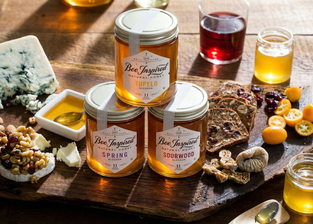 Three jars of 'Bee Inspired' royale honey on a wooden board with snacks and drinks.

