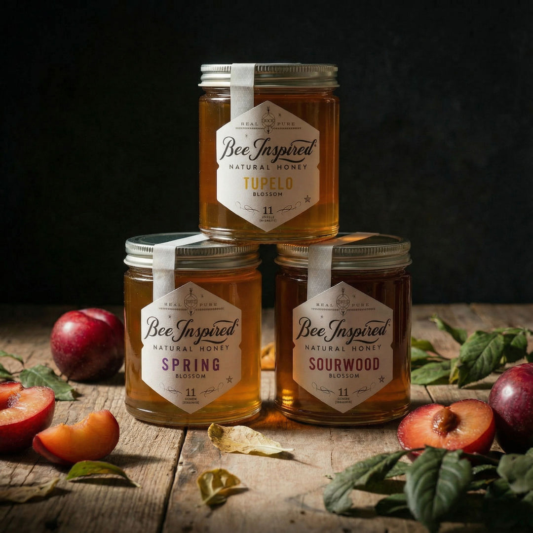 Three jars of Bee Inspired Royal honey on a wooden surface with fresh-picked and cut plums and leaves.