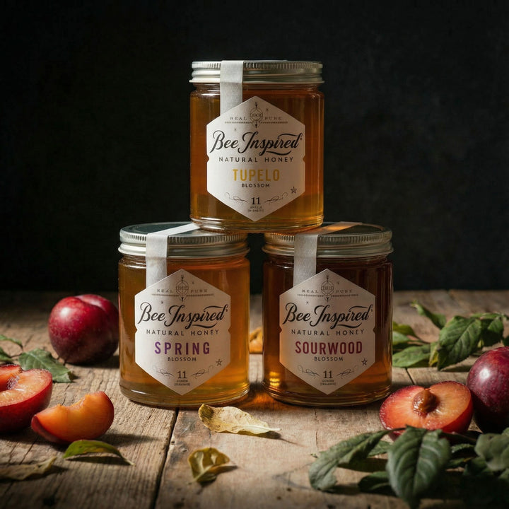 Three jars of Bee Inspired Royal honey on a wooden surface with fresh-picked and cut plums and leaves.