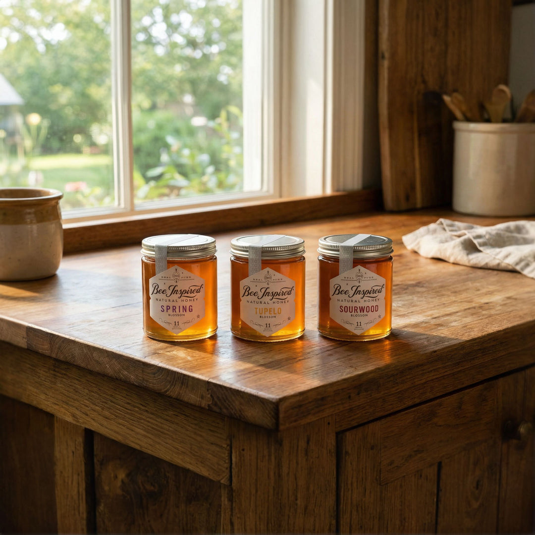 Three jars of honey on a wooden surface with a window in the background