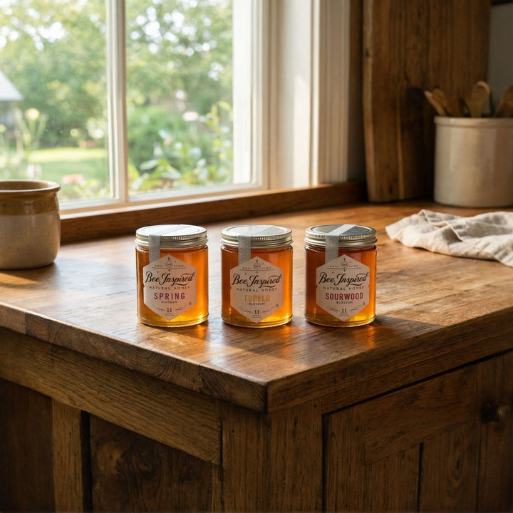 Three jars of honey on a wooden surface with a window in the background