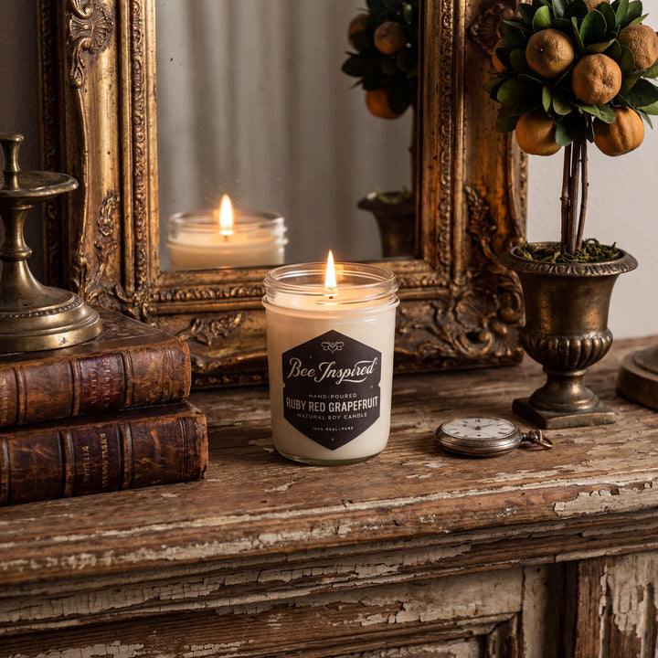 Candle jar labeled 'Bee Inspired' with 'Ruby Red Grapefruit' scent on an antique mantle