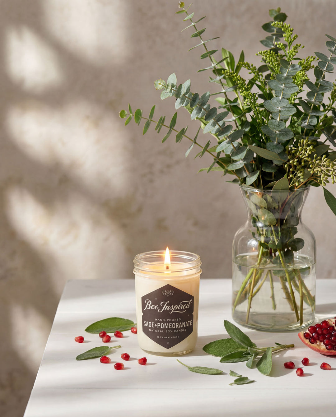 Candle with a label and a vase of greenery on a table