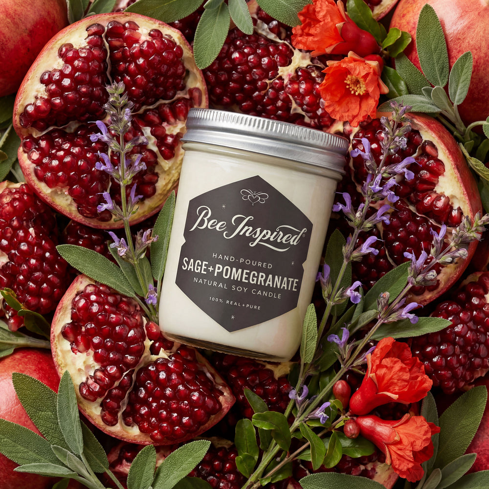 Candle labeled 'Bee Inspired' surrounded by pomegranates, sage, and flowers