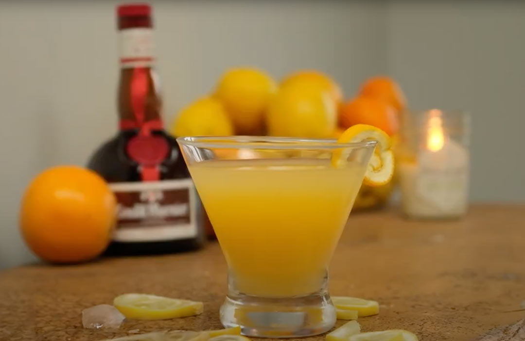 orange honey screwdriver in front of oranges and bottle of alcohol 