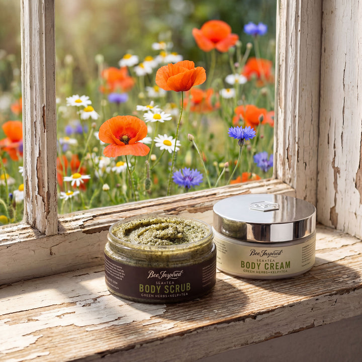 Two jars of body scrub and cream on a windowsill with a view of flowers outside.