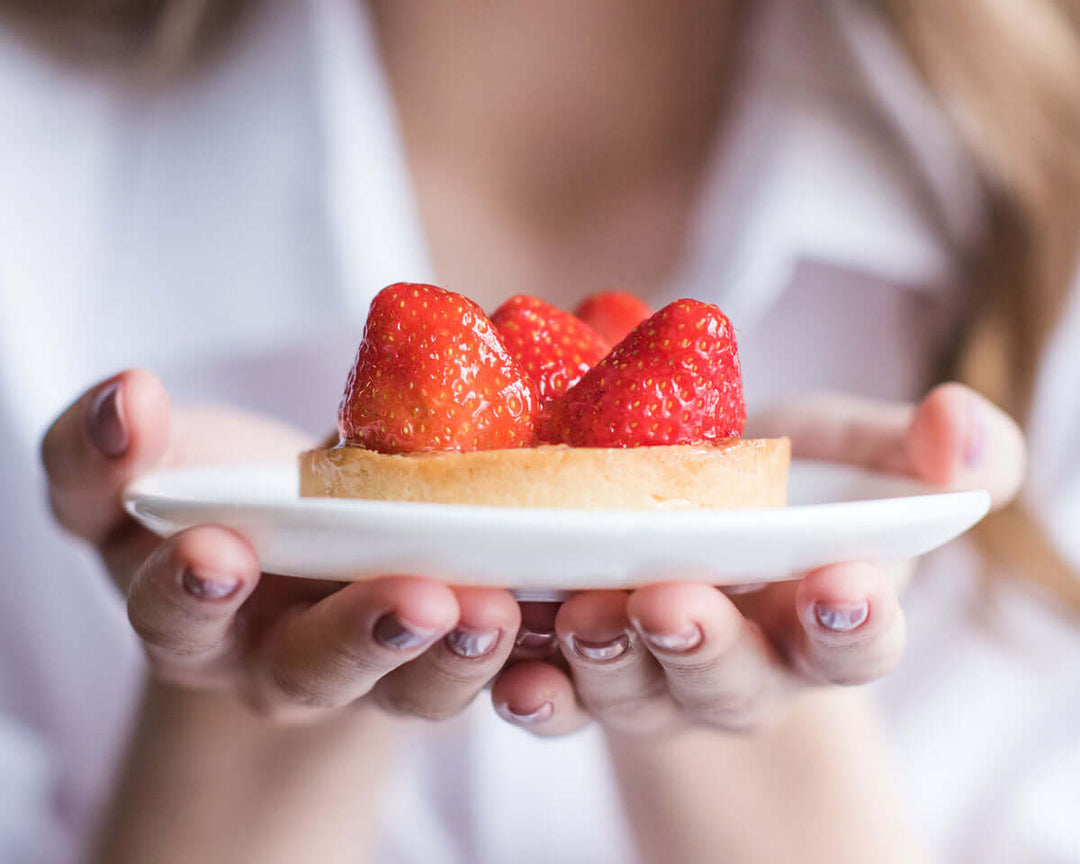 hands holding out a plate with a pastry topped with strawberries