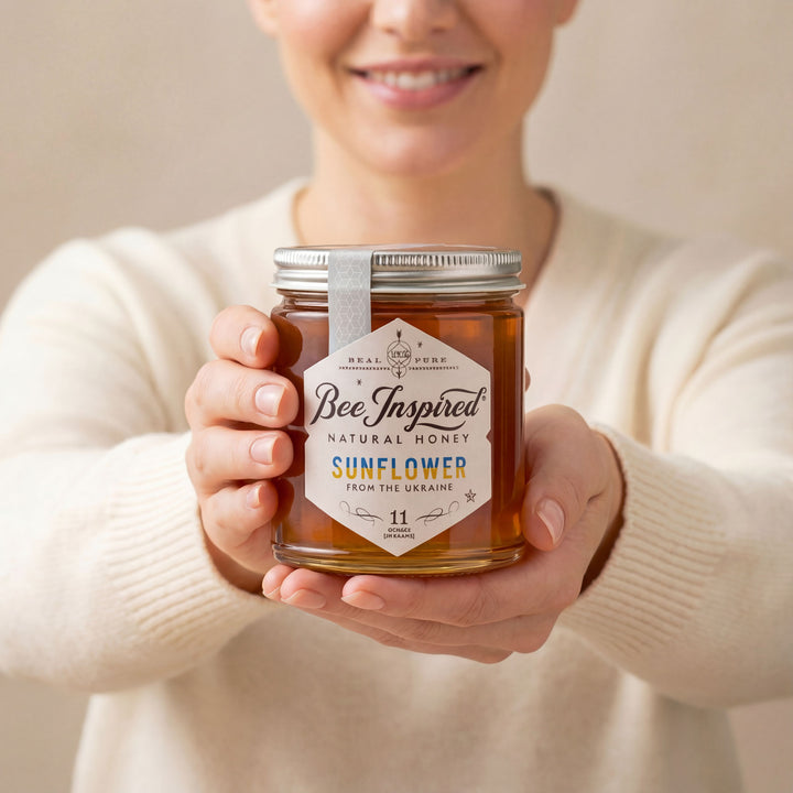 Person holding a jar of 'Bee Inspired' sunflower honey with a neutral background