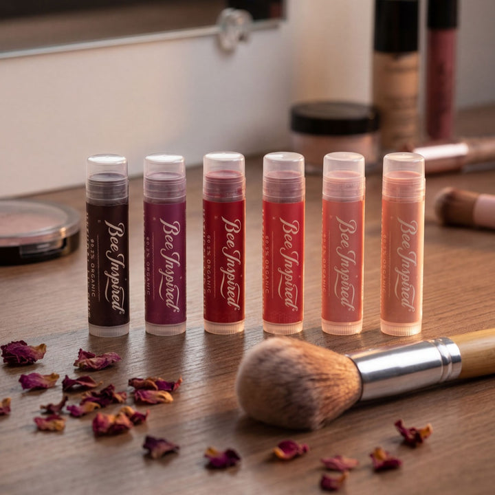 Set of lip balms with visible brand name on a wooden surface with makeup tools.